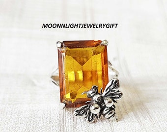 May include: A silver ring with a large, rectangular, amber-colored gemstone and a small silver bee charm.