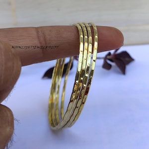 May include: Set of five gold-toned hammered metal bangles. The bangles are stacked on top of each other and are slightly curved.