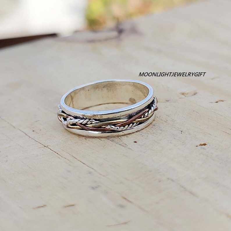 Pu&ograve; includere: Un anello a fascia d'argento con un design intrecciato con accenti in rame e oro.