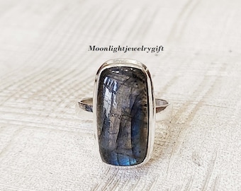 Può includere: Un anello d'argento con una pietra rettangolare di labradorite blu iridescente.