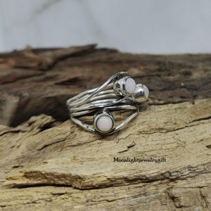 Pu&ograve; includere: Un anello d'argento con tre pietre di opale bianco incastonate in un design a filo ritorto.