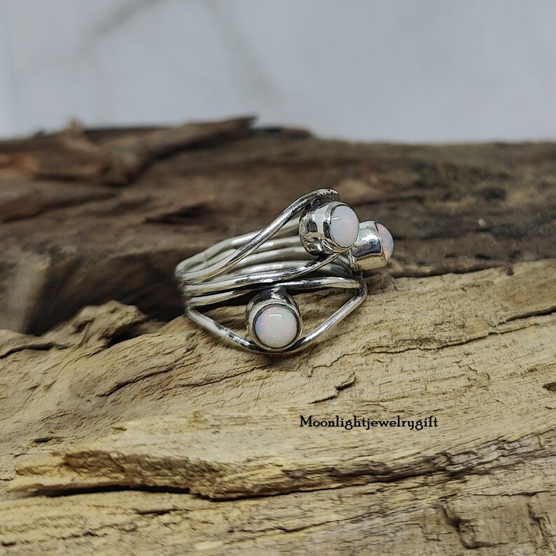 Pu&ograve; includere: Un anello d'argento con tre pietre di opale bianco incastonate in un design a filo ritorto.