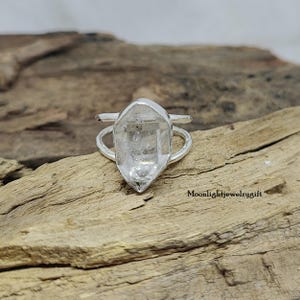 May include: A silver ring with a clear quartz crystal set in the center. The ring is designed to be worn on the knuckle.