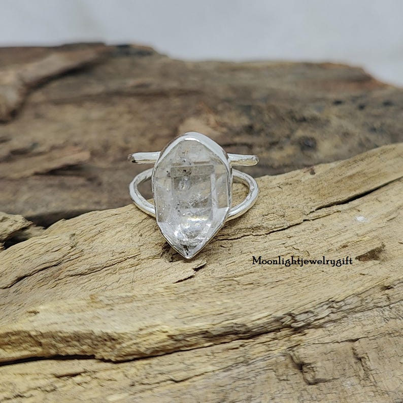 May include: A silver ring with a clear quartz crystal set in the center. The ring is designed to be worn on the knuckle.