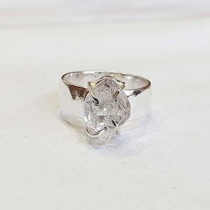 May include: A silver ring with a clear quartz crystal set in the center. The crystal is faceted and has a unique shape.