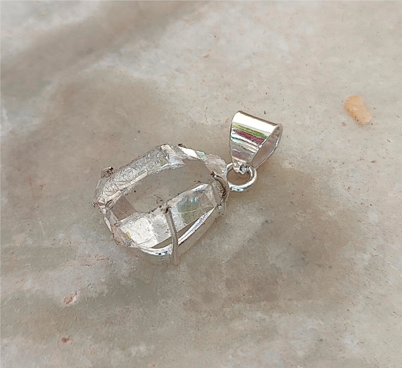May include: A clear quartz crystal pendant with a silver setting. The crystal is faceted and has a natural, rough appearance. The pendant is attached to a silver bail.
