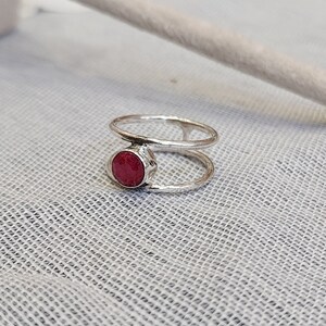 Może przedstawiać: Srebrny pierścionek z czerwonym kamieniem szlachetnym osadzonym w środku. Pierścionek ma podw&oacute;jny wz&oacute;r.