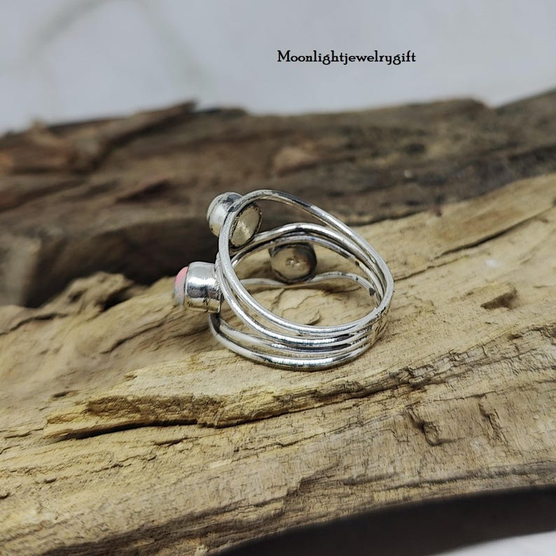 Pu&ograve; includere: Un anello d'argento con tre bande e due pietre rosa. L'anello &egrave; su una superficie di legno.