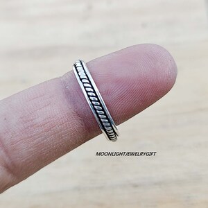 May include: A silver ring with a braided design. The ring is on a finger.