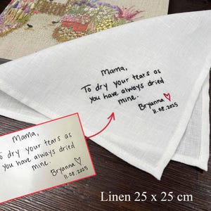 K&ouml;nnte beinhalten: Ein wei&szlig;es Leinentaschentuch mit den Ma&szlig;en 25 x 25 cm, bestickt mit schwarzem Text: Mama, To dry your tears as you have always dried mine. Bryanna, gefolgt von einem roten Herz und dem Datum 11.08.2025, passend zu einer unten gezeigten Notiz.