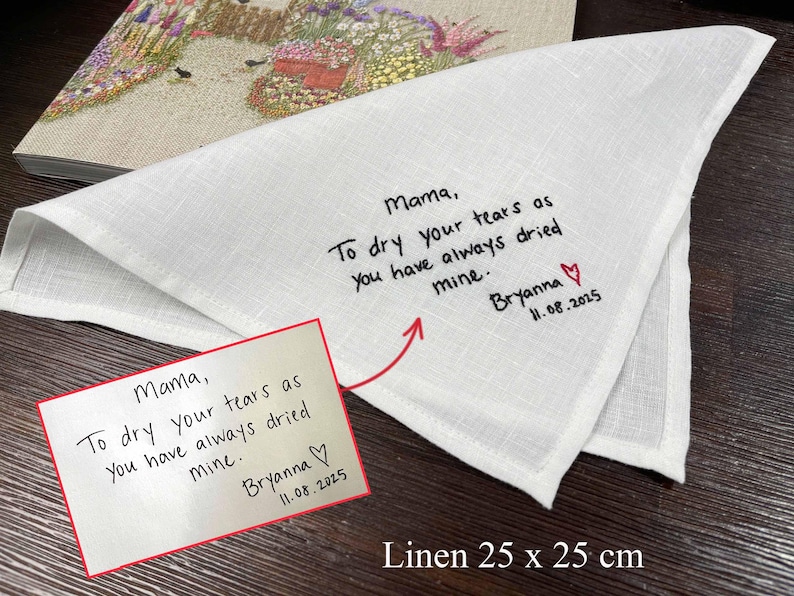 K&ouml;nnte beinhalten: Ein wei&szlig;es Leinentaschentuch mit den Ma&szlig;en 25 x 25 cm, bestickt mit schwarzem Text: Mama, To dry your tears as you have always dried mine. Bryanna, gefolgt von einem roten Herz und dem Datum 11.08.2025, passend zu einer unten gezeigten Notiz.