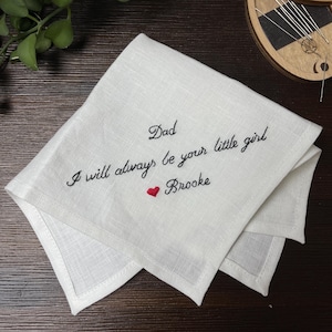 K&ouml;nnte beinhalten: Ein wei&szlig;es, quadratisches Leinentaschentuch mit schwarzer, gestickter Schreibschrift, die Dad I will always be your little girl lautet, gefolgt von einem kleinen roten gestickten Herz und dem Namen Brooke in schwarzer Schreibschrift.