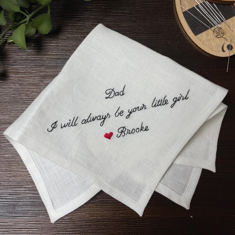 K&ouml;nnte beinhalten: Ein wei&szlig;es, quadratisches Leinentaschentuch mit schwarzer, gestickter Schreibschrift, die Dad I will always be your little girl lautet, gefolgt von einem kleinen roten gestickten Herz und dem Namen Brooke in schwarzer Schreibschrift.