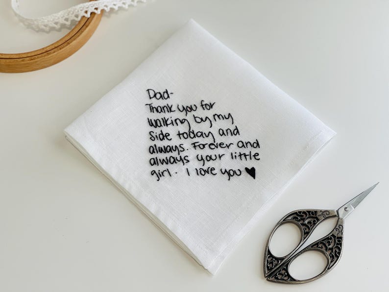 K&ouml;nnte beinhalten: Ein wei&szlig;es quadratisches Taschentuch mit schwarzem gesticktem Text: Dad- Thank you for walking by my side today and always. Forever and always your little girl. I love you, gefolgt von einem kleinen schwarzen gestickten Herzsymbol.