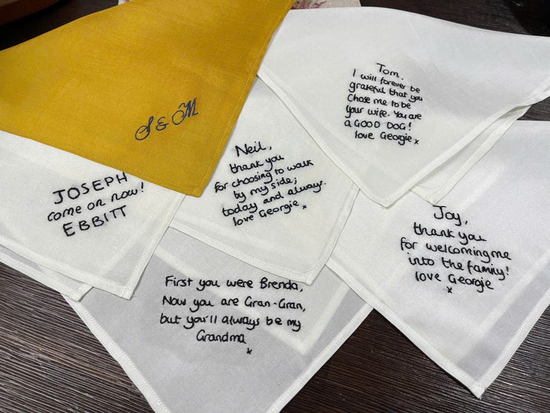 K&ouml;nnte beinhalten: Eine Sammlung von wei&szlig;en und einem senfgelben Stofftaschentuch mit schwarzem Sticktext. Die Nachrichten enthalten pers&ouml;nliche Notizen und Namen wie Joseph, Neil, Tom, Joy und Brenda sowie ein Monogramm S & M auf dem gelben Tuch.