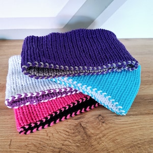 May include: Four knitted headbands stacked on top of each other. The top headband is purple with a gray trim, the second headband is white with a purple trim, the third headband is turquoise with a white trim, and the bottom headband is pink with a black trim.