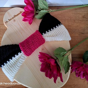 Könnte beinhalten: Zwei gestrickte Stirnbänder in Schwarz, Weiß und Pink auf einer Holzoberfläche. Die Stirnbänder sind in Form einer Schleife angeordnet. Der Text "sk.headbands" ist in die Holzoberfläche graviert.