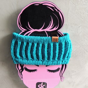 Könnte beinhalten: Ein türkisfarbenes gestricktes Stirnband mit einem braunen Lederanhänger, auf dem "MADE WITH LOVE" steht.