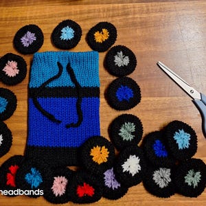 Könnte beinhalten: Eine Sammlung bunter Strickhaarbänder in verschiedenen Farben, darunter Blau, Rosa, Gelb und Grün. Die Haarbänder sind in einem Kreis um ein gestricktes Haarbänder mit blau-schwarzem Streifenmuster angeordnet. Der Text "sk.headbands" ist in der linken unteren Ecke des Bildes sichtbar.
