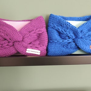 May include: Two knitted headbands, one pink and one blue, with a knotted design. Both headbands have a white tag with the text "sk.headbands" on them.