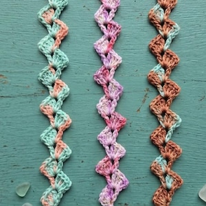 May include: Three crocheted bookmarks featuring a wavy, zigzag pattern. The first is mint green and peach, the second is variegated pink and purple, and the third is brown and light blue. Each bookmark has a small silver bead at both ends.