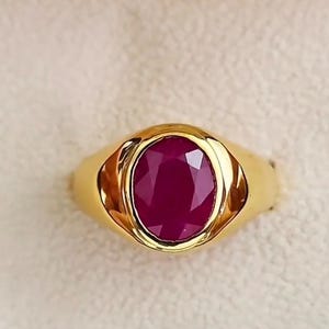Op de afbeelding: Een gouden ring met een grote, ovaal geslepen robijn. De robijn heeft een dieprode kleur en is gezet in een gepolijste gouden band. De ring heeft een klassiek, elegant ontwerp.
