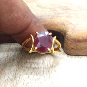 以下が含まれることがあります： 大きなオーバルカットのルビーの宝石をあしらったゴールドカラーのリング。 ルビーは深い赤色で、リングの焦点となっています。 リングのバンドは、湾曲したアクセントを持つユニークなデザインです。