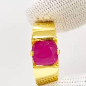 以下が含まれることがあります： 大きな楕円形にカットされたマゼンタ色の宝石をあしらったゴールドリング。長方形のバンドとベゼルセッティングを備えたシンプルでモダンなデザインです。宝石は焦点であり、鮮やかな色と輝きを際立たせています。