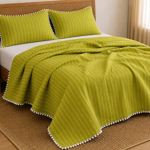 May include: A lime green bedding set consisting of a quilt and two matching pillow shams. The fabric features a subtle vertical striped texture and is finished with a decorative white pom-pom trim along the edges of the quilt and pillows.
