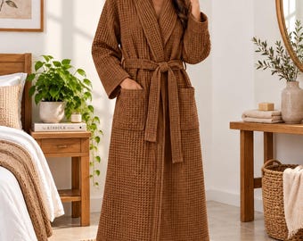 May include: A long, brown waffle-textured robe featuring a shawl collar, long sleeves, two front patch pockets, and a matching fabric tie belt at the waist. The garment is constructed with a grid-like pattern throughout the fabric.