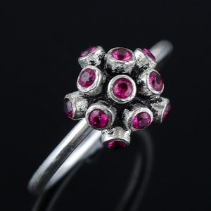 Può includere: Un anello per il naso in argento con un gruppo di pietre preziose rosa. L'anello è fatto di due sottili bande di metallo che sono intrecciate insieme.