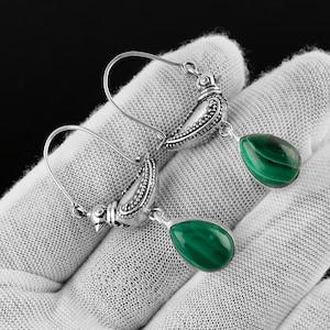 Puede incluir: Pendientes de plata con diseño de pájaro. Cada pendiente presenta una piedra de malaquita verde en forma de lágrima. Los pendientes se muestran sobre una superficie blanca.