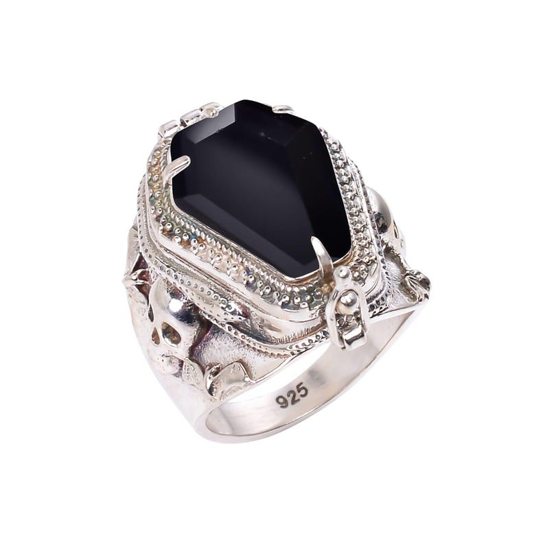 May include: A silver ring with a black gemstone set in a detailed, ornate design. The ring features a skull motif and the inscription "925" on the band.