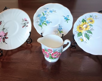 Juego de platillos y mini jarra de crema de porcelana inglesa con borde dorado y diseño floral.