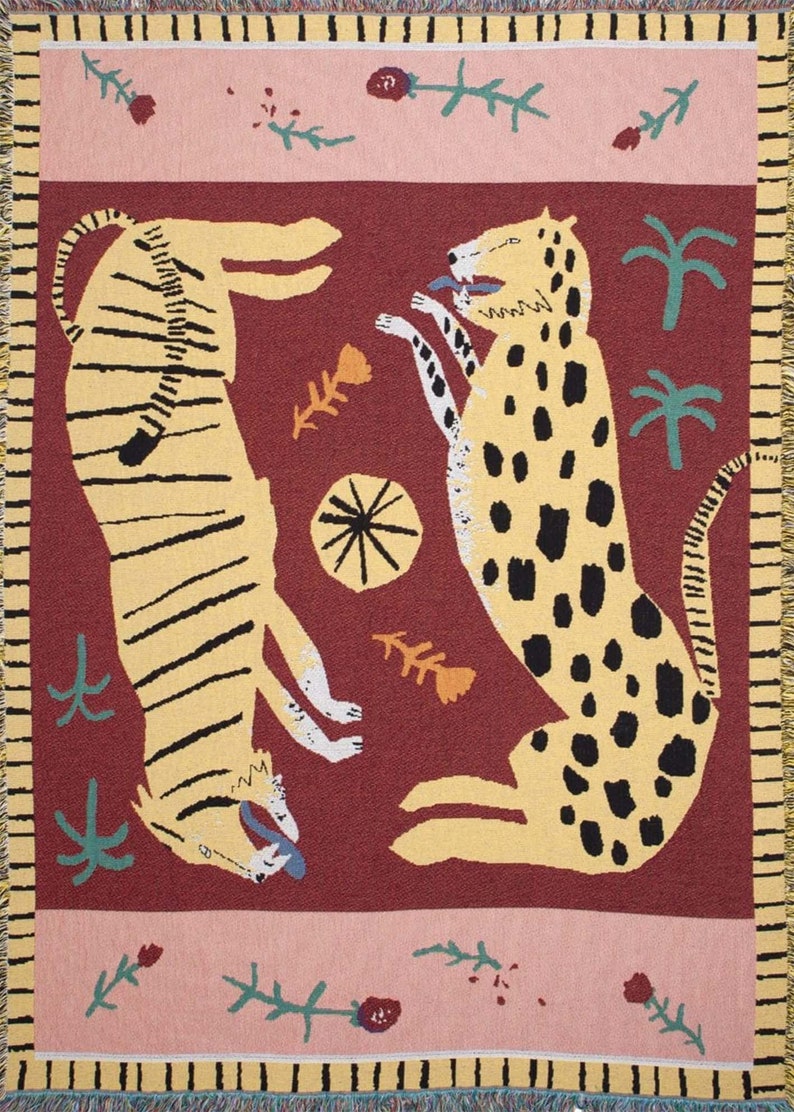 May include: A woven tapestry featuring two stylized animals, a tiger and a leopard, in a playful pose against a burgundy background. The tapestry is framed by a pink border with green floral accents.