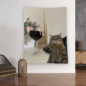 Może przedstawiać: Koty tabby siedzi na krześle z kieliszkiem czerwonego wina na stole przed nim. Kot patrzy w obiektyw z poważnym wyrazem twarzy. W tle znajduje się bukiet r&oacute;żowych kwiat&oacute;w.