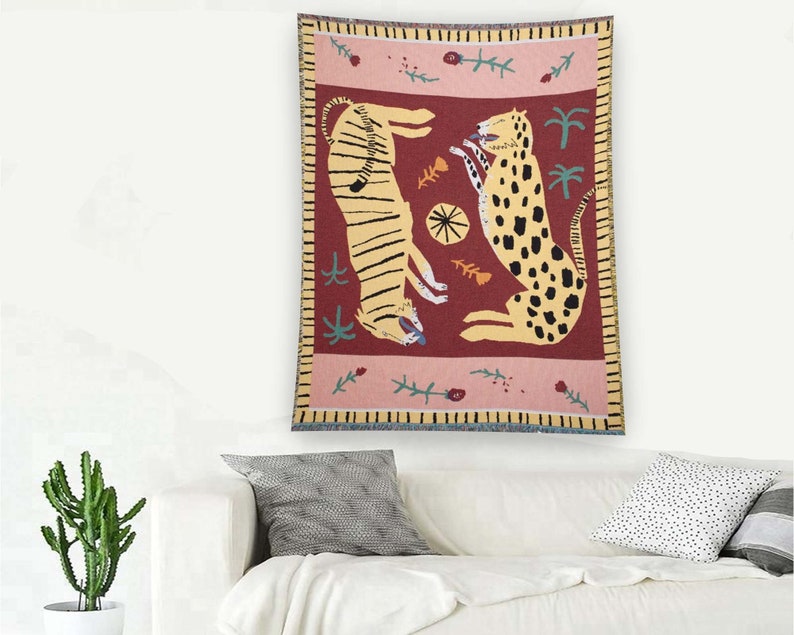 May include: A tapestry featuring a red background with two stylized animals, a tiger and a leopard, in yellow and brown. The tapestry has a pink and yellow border with floral and leaf designs.