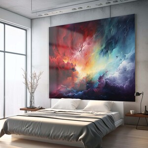 May include: A bedroom with a large abstract painting of colorful clouds hanging on the wall above a gray bed with white bedding. The painting features shades of red, orange, yellow, blue, and purple.