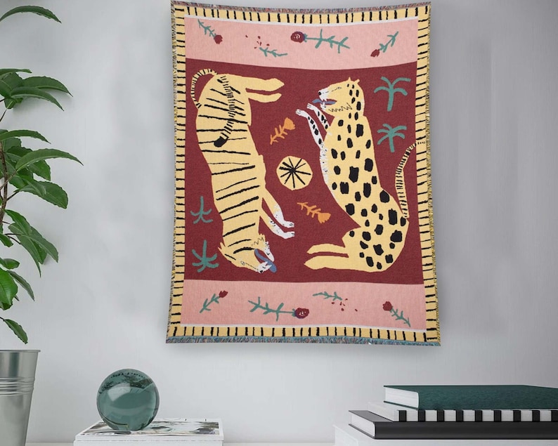 May include: A woven tapestry wall hanging with a red background featuring a yellow and black tiger and a yellow and brown leopard. The tapestry has a pink border with green floral accents.