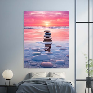 Puede incluir: Una pila de piedras grises lisas, equilibradas una encima de la otra en el agua poco profunda de una playa al atardecer. El cielo es de un rosa y naranja vibrantes, y el agua es de un azul claro.
