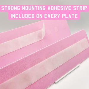 May include: Close-up of pink plates with strong mounting adhesive strips. The text on the image reads: "STRONG MOUNTING ADHESIVE STRIP INCLUDED ON EVERY PLATE."