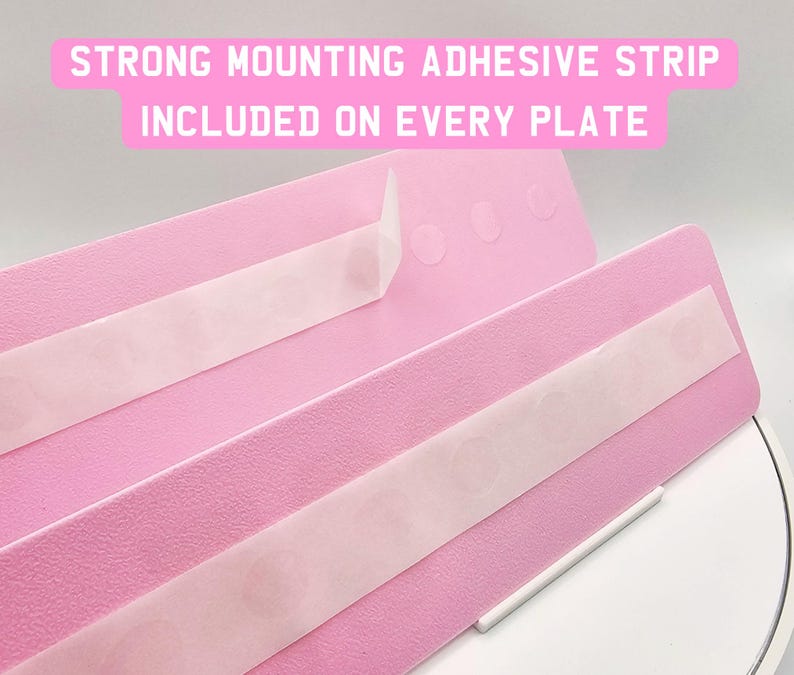 May include: Close-up of pink plates with strong mounting adhesive strips. The text on the image reads: "STRONG MOUNTING ADHESIVE STRIP INCLUDED ON EVERY PLATE."