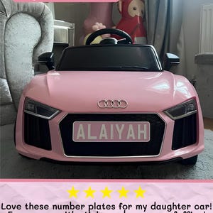 May include: A pink toy car with a black interior and the name "ALAIYAH" on a license plate. The car has the Audi logo on the front. The text "Large Plate Example" is at the top of the image.