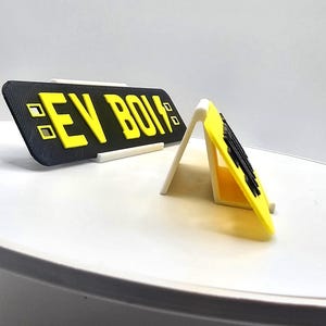 May include: A black and yellow sign with the text "EV BOIS" in yellow block letters. The sign is displayed on a white stand. The sign is rectangular and has a matte finish.