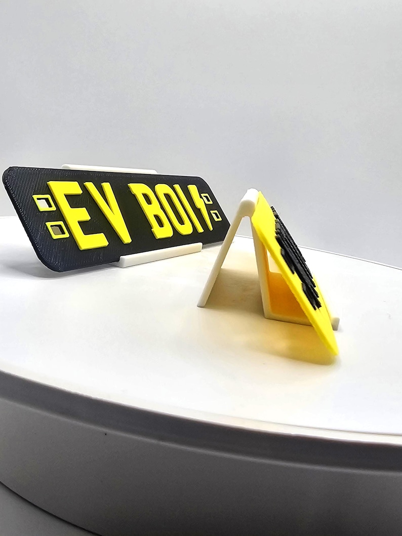 May include: A black and yellow sign with the text "EV BOIS" in yellow block letters. The sign is displayed on a white stand. The sign is rectangular and has a matte finish.
