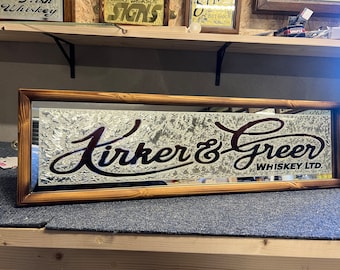 Könnte beinhalten: Ein Holzrahmenspiegel mit silbernem Hintergrund und einem schwarzen und roten kursiven Logo mit der Aufschrift "Kirker & Greer Whiskey LTD."