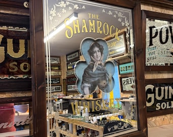 Könnte beinhalten: Ein Vintage-Spiegel in einem Holzrahmen mit einer goldenen Inschrift, die "The Shamrock Whiskey" lautet, und einem Frauenporträt in einem blauen Kleeblatt. Die Inschrift enthält auch "Gegründet 1885".