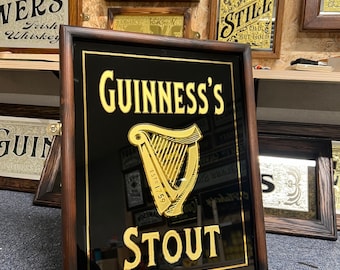 Könnte beinhalten: Ein dunkelbrauner, mit Holz gerahmter Spiegel mit schwarzem Hintergrund und goldenen Buchstaben. Der Spiegel zeigt "GUINNESS'S" mit einem goldenen Harfenlogo und "ESTD 1759" unter der Harfe. Der Text "STOUT" befindet sich unter der Harfe und dem Jahr.