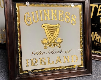 Könnte beinhalten: Ein gerahmter Spiegel mit einem goldenen Guinness-Logo und dem Text "The Taste of Ireland". Der Rahmen ist aus dunkelbraunem Holz.