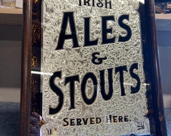 Könnte beinhalten: Ein gerahmter Spiegel mit schwarzem Hintergrund und goldenen Akzenten. Der Spiegel hat ein silbernes Prägemuster mit dem Text "Irish Ales & Stouts Served Here."